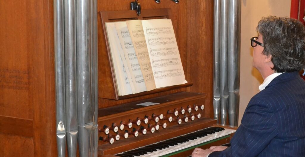 Immagine di un uomo che suona un organo storico Callido durante un concerto, con musica aperta di fronte.